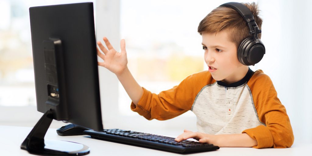 Poika pelaa tietokoneella videopeliä kuulokkeet päässä.