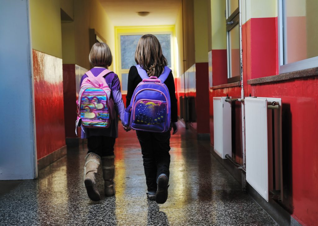 Kaksi pientä opiskelijalasta kävelemässä koulun käytävää pitkin.