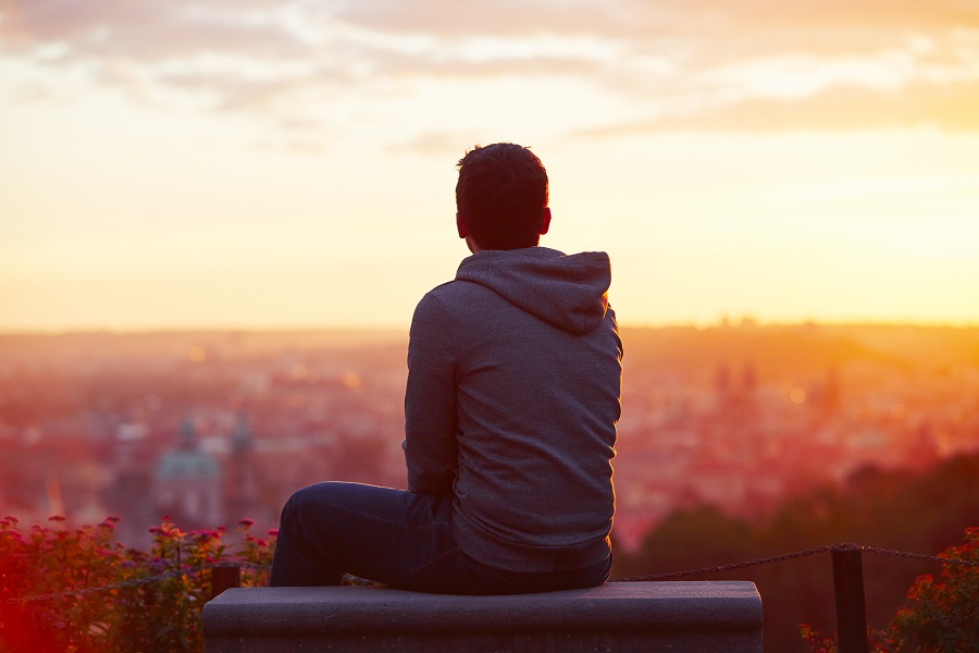 Mies istuu penkillä ja katsoo kaupungin yli auringonnousua.