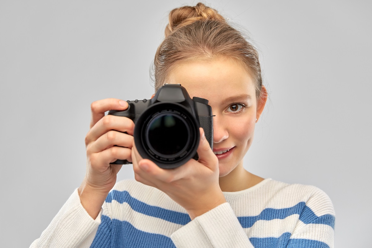 Hymyilevä nuori nainen kuvaa digikameralla.