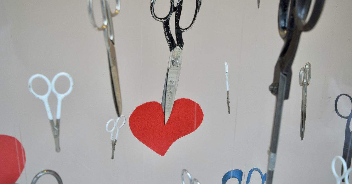 Ilmassa leijuu saksia, joista yksi leikkaa paperisen sydämen kahtia.